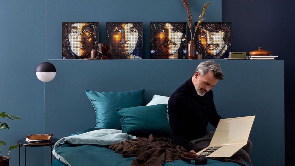 man sitting in living room looking at a book with LEGO art behind him