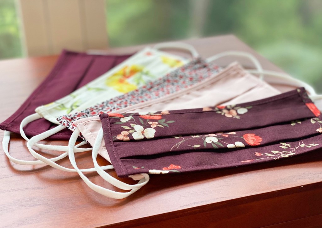 five resuable face masks in various floral prints on wood table