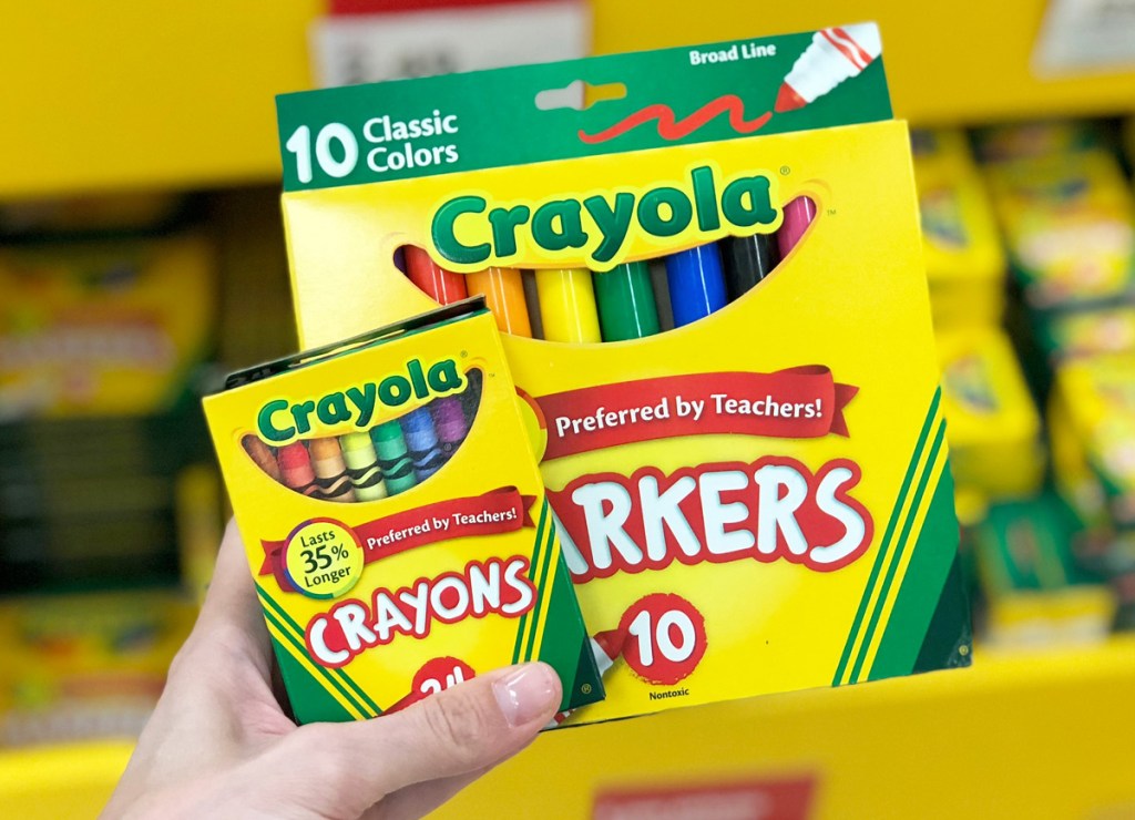 person holding yellow and green boxes of crayola crayons and markers