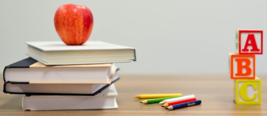 books, apple, pencils, and letter blocks on desk