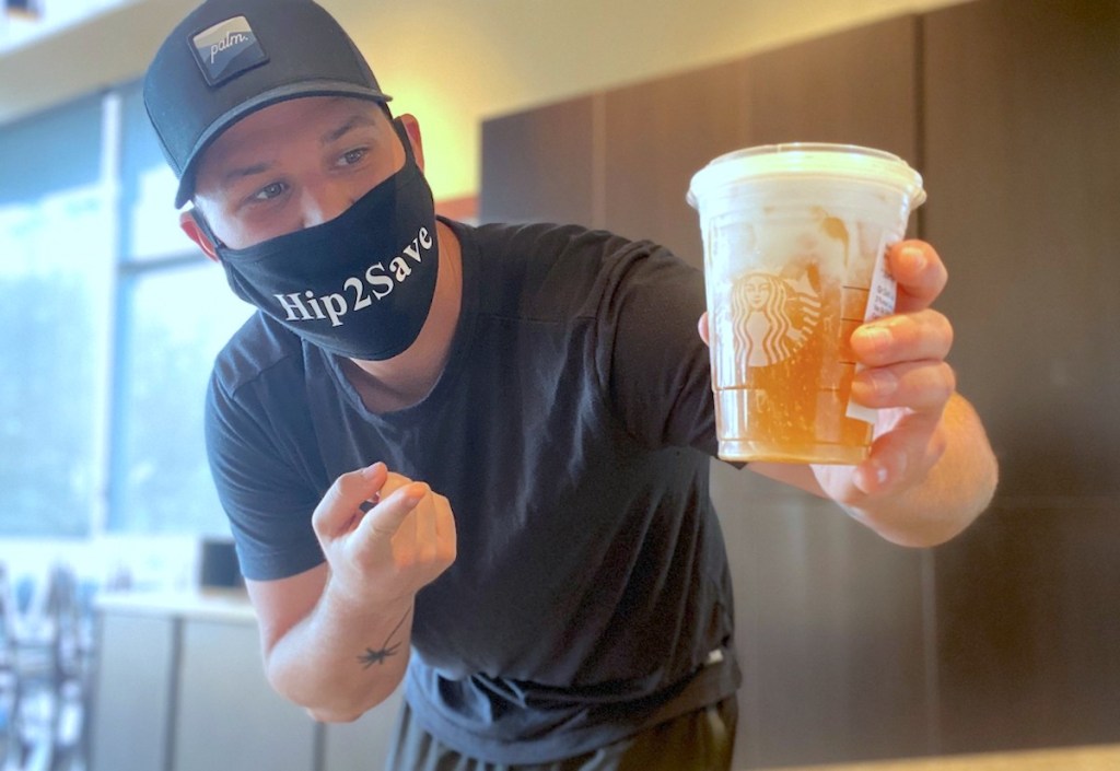 man wearing a hip2save mask holding a starbucks drink with half orange and white 