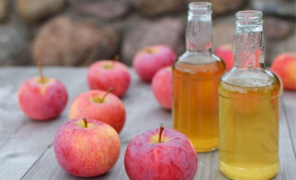 Jugs of homemade apple cider next to a few apples