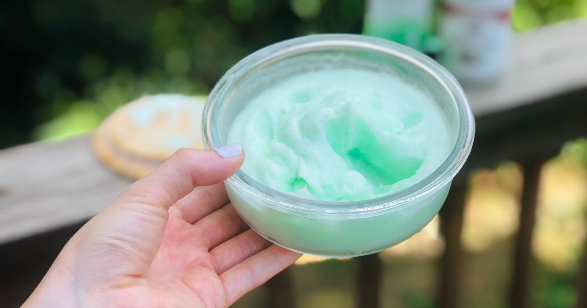 Fingers with whipped cream lotion on fingertips with products on deck railing in background