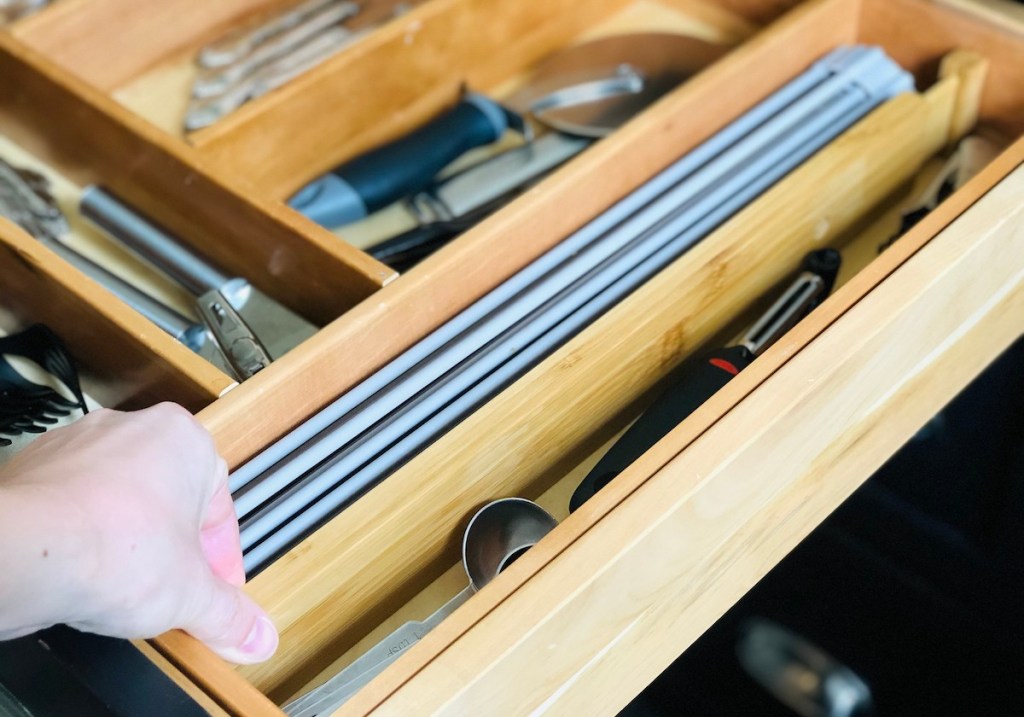 hand holding end of wood drawer divider with kitchen utensils inside