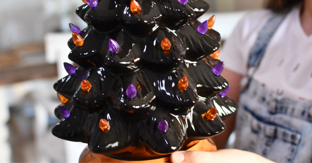 person holding a black tree with orange and purple lights on it