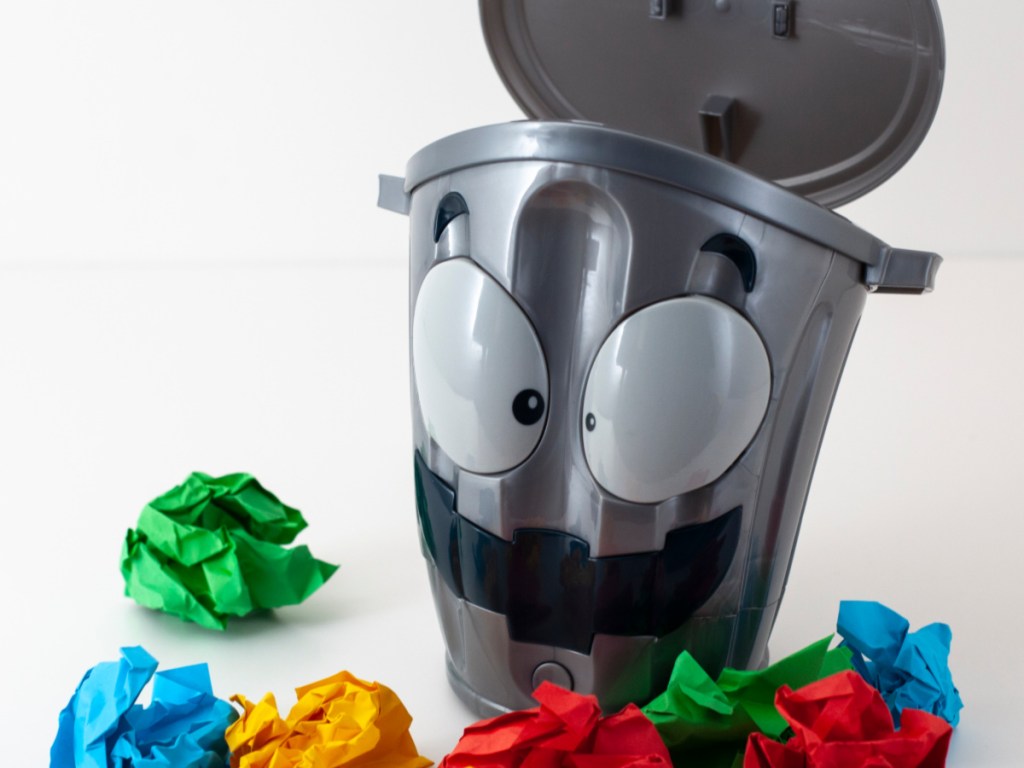 silver trash can with face on it surrounded by colored balls of paper