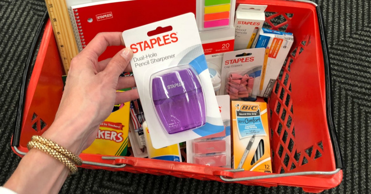 hand holding a pencil sharpener package over a basket full of school supplies