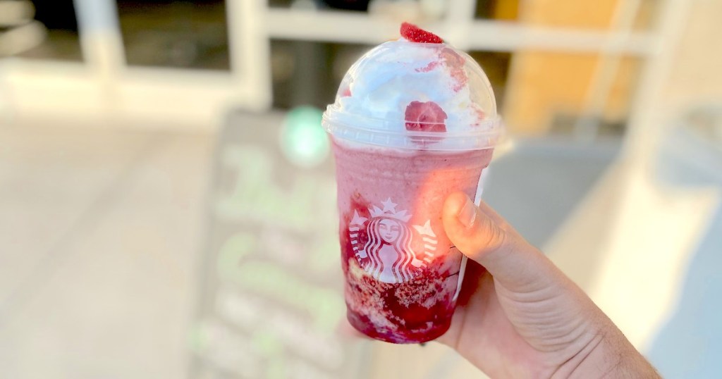 hand holding a pink strawberry starbucks drink outside of store front