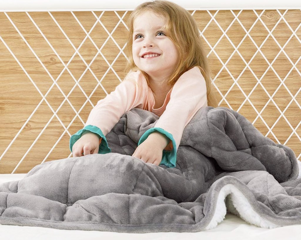 girl in pink pajamas under a grey sherpa fleece weighted blanket