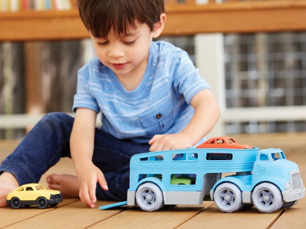 boy playing with vehicle toy set on hardwood floor