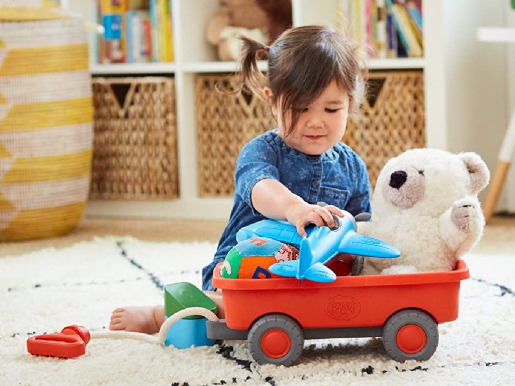 girl playing with orange wagon and other toys on carpet