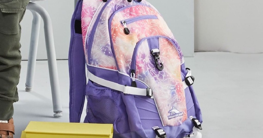 purple and pink print backpack on floor by school desk