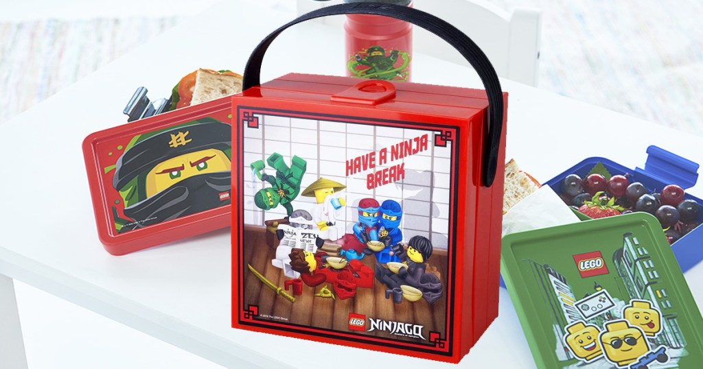 square red LEGO Ninjago lunchbox with other LEGO lunchboxes on table behind it