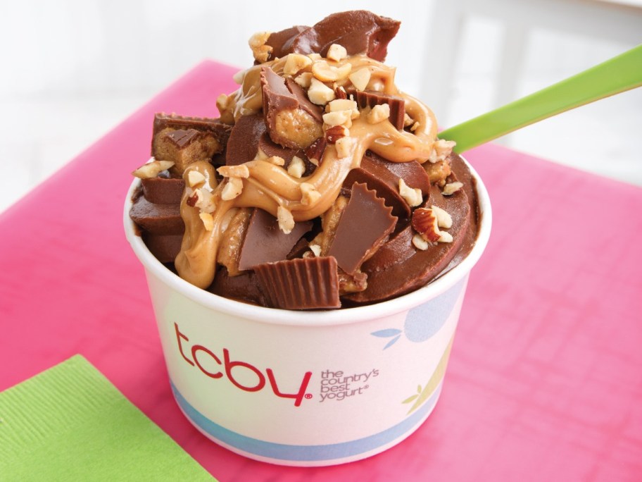 cup of chocolate frozen yogurt topped with peanut butter cup candies, peanut butter sauce, and peanuts