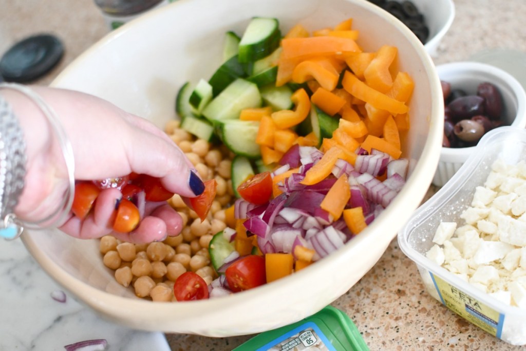 adding tomatoes to greek chickpea salad