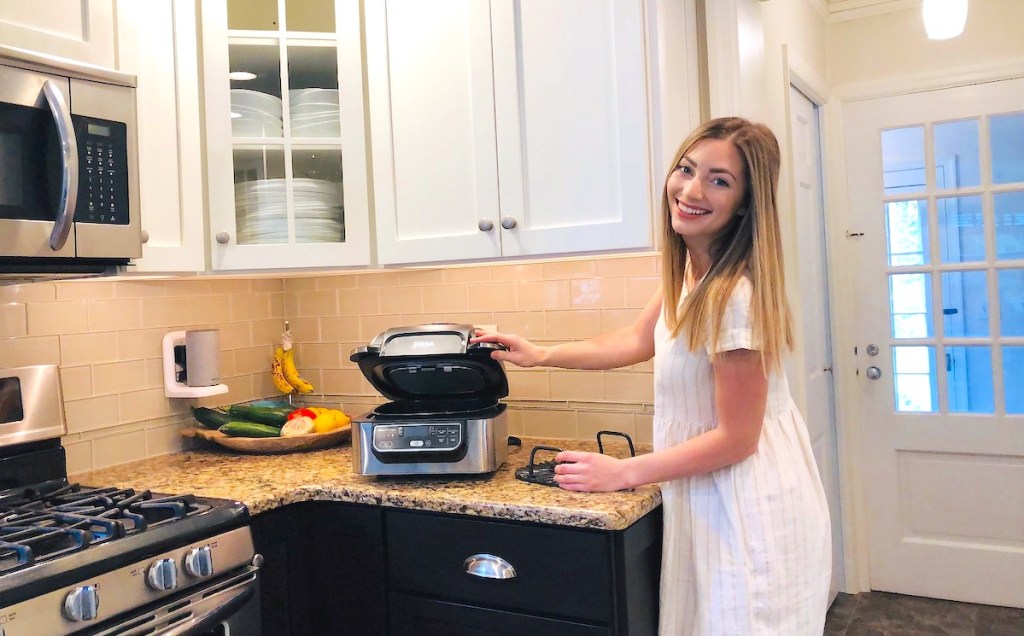 woman standing next to ninja foodi indoor grill sitting on kitchen countertop