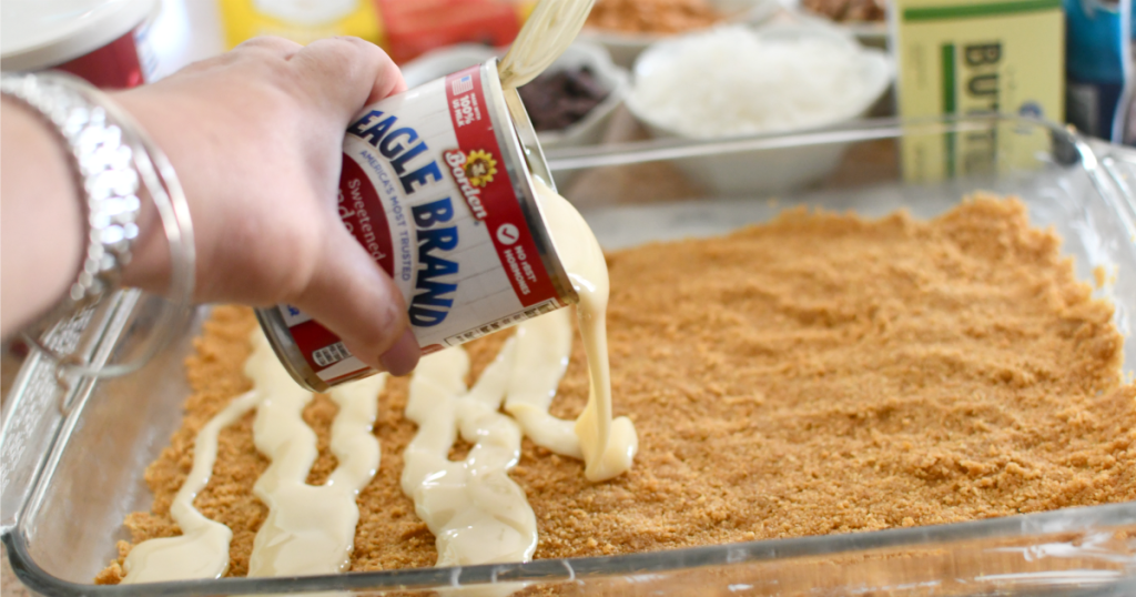 pouring a can of condensed milk over magic cookie bars