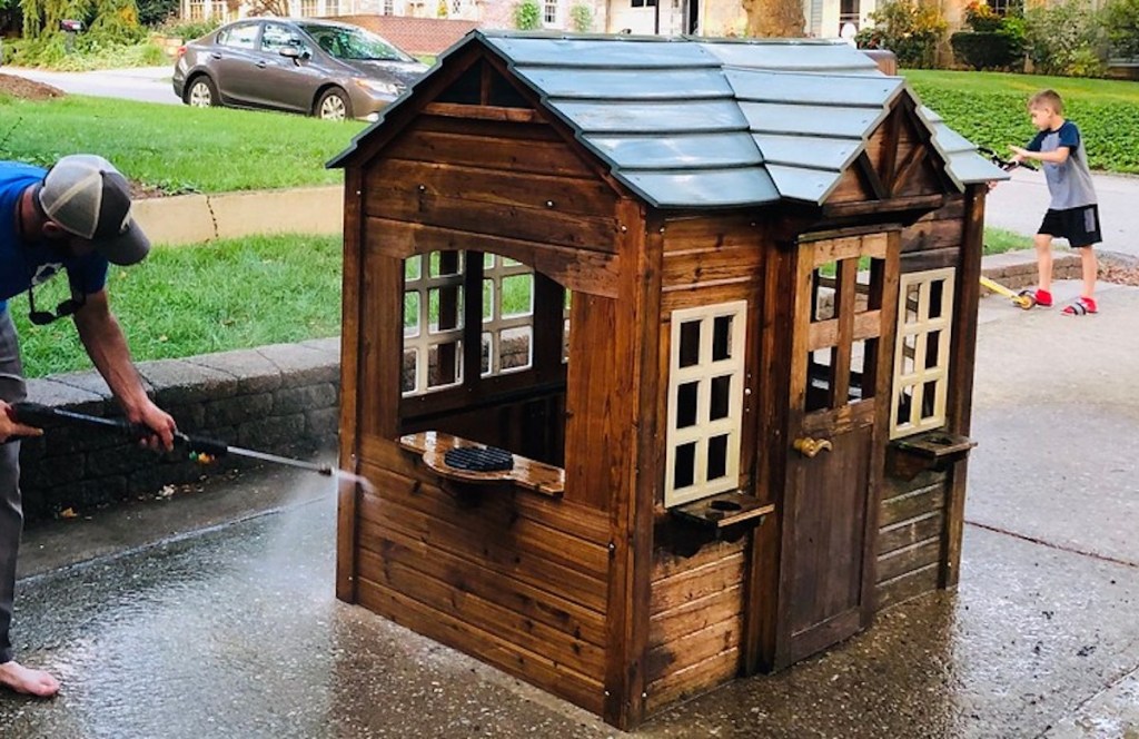 man power washing kids playhouse in driveway