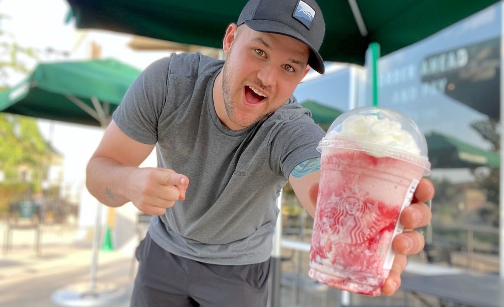 man holding a starbucks skittles frappuccino outside