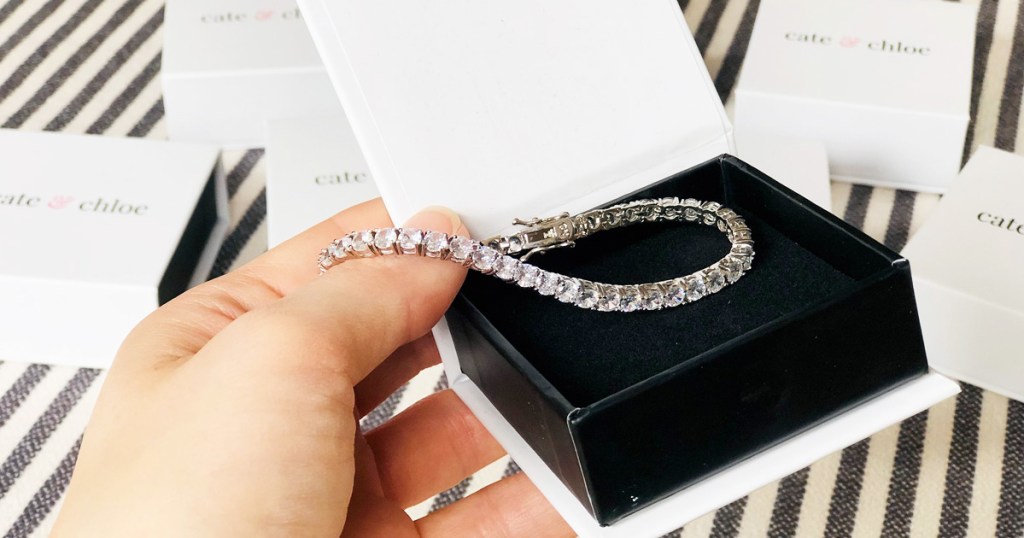 person holding up a white and black jewelry box with a white gold tennis bracelet inside