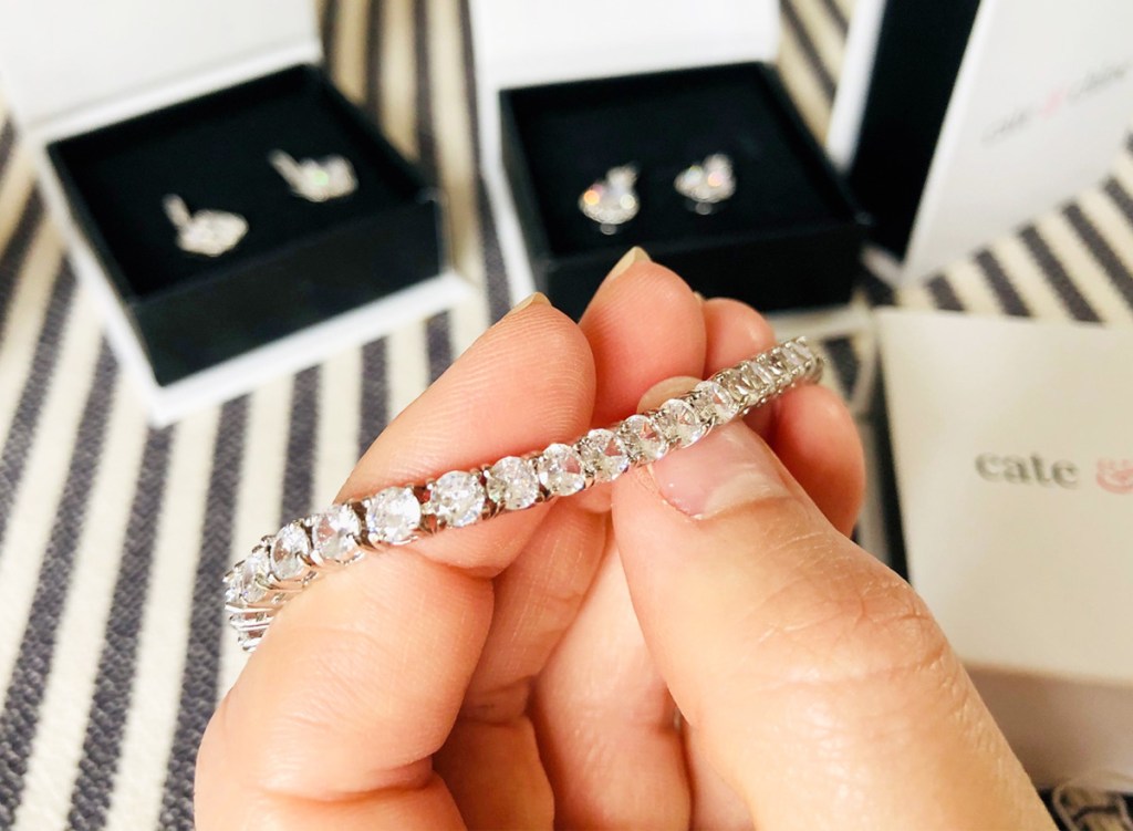 person holding up a white gold tennis bracelet with other jewelry boxes in background