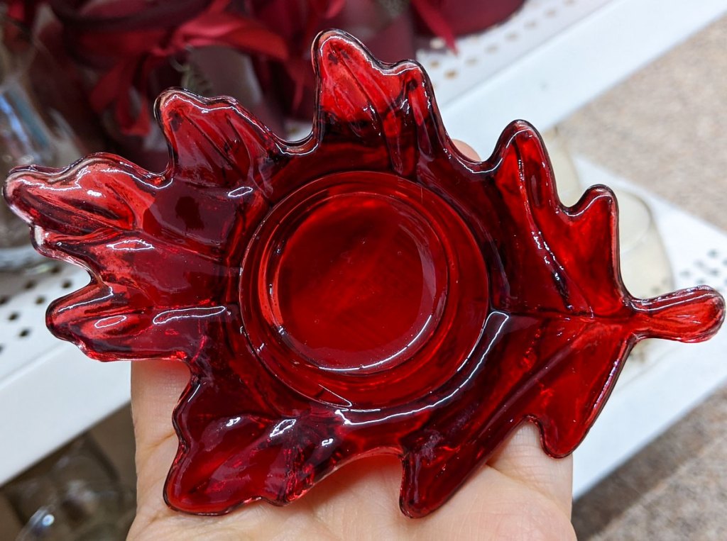 person holding a red leaf shaped tealight candle holder in palm of their hand