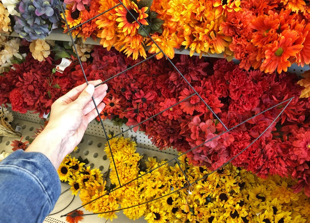 person holding up halloween witch's hat shaped wire wreath form in front of silk flowers