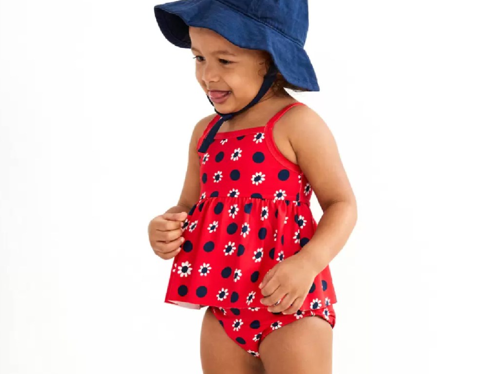 toddler girl wearing a 2-piece red swimsuit and blue bucket hat