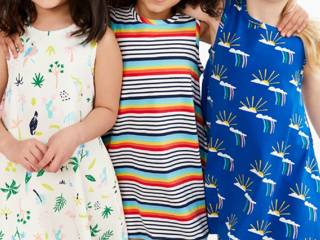 3 little girls standing next to each other wearing colorful sleeveless dresses