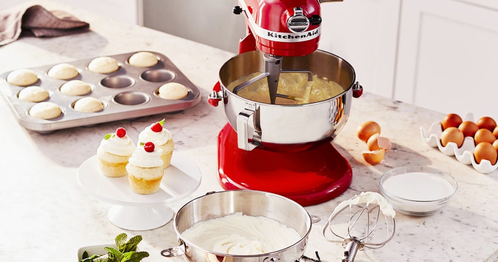 red KitchenAid mixer on counter with cupcakes and baking ingredients around it