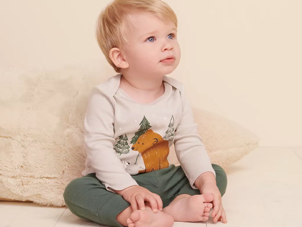 baby boy sitting on the ground wearing a woodland onesie and green pants