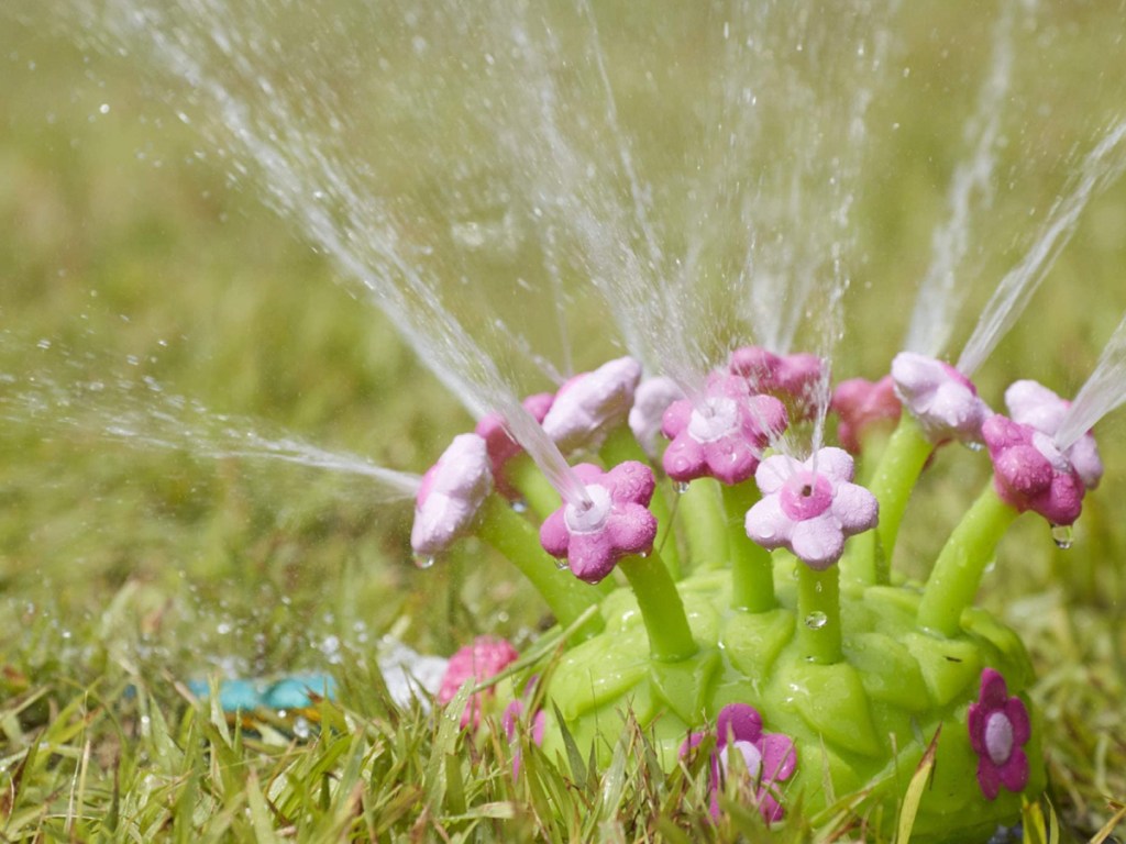 pink and green plastic sprinkler spouting water and sitting in the grass