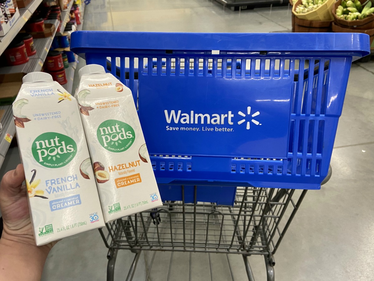 Hand holding two containers of nutpods creamer near a Walmart shopping basket