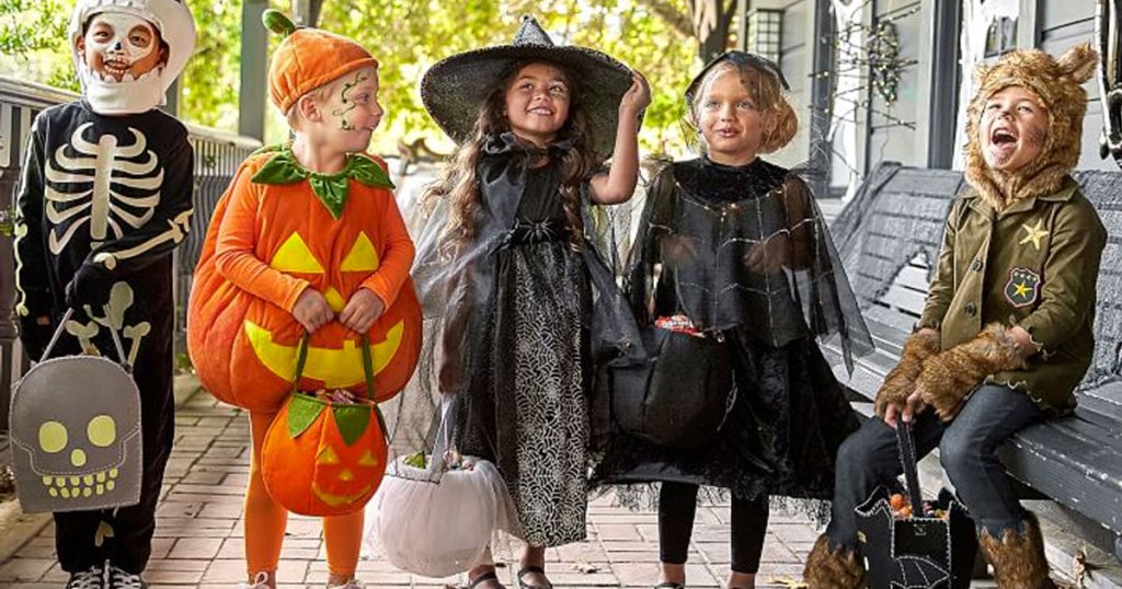 group of kids standing outside dressed in halloween costumes and holding treat bags