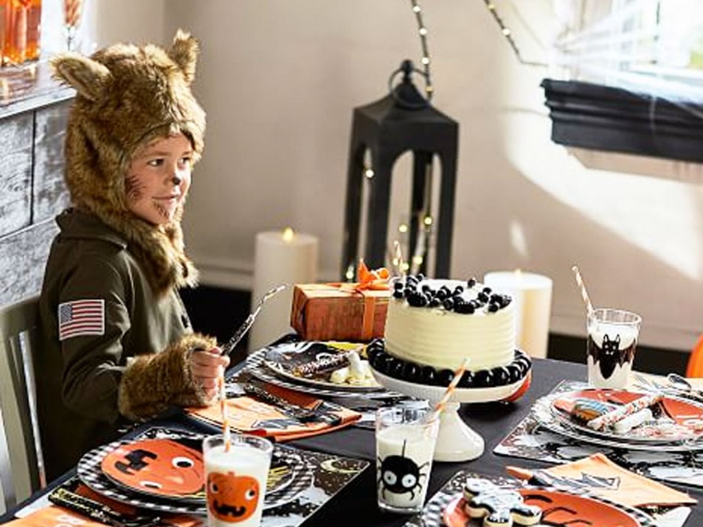 boy dressed in werewolf halloween costume sitting at a table with halloween party supplies