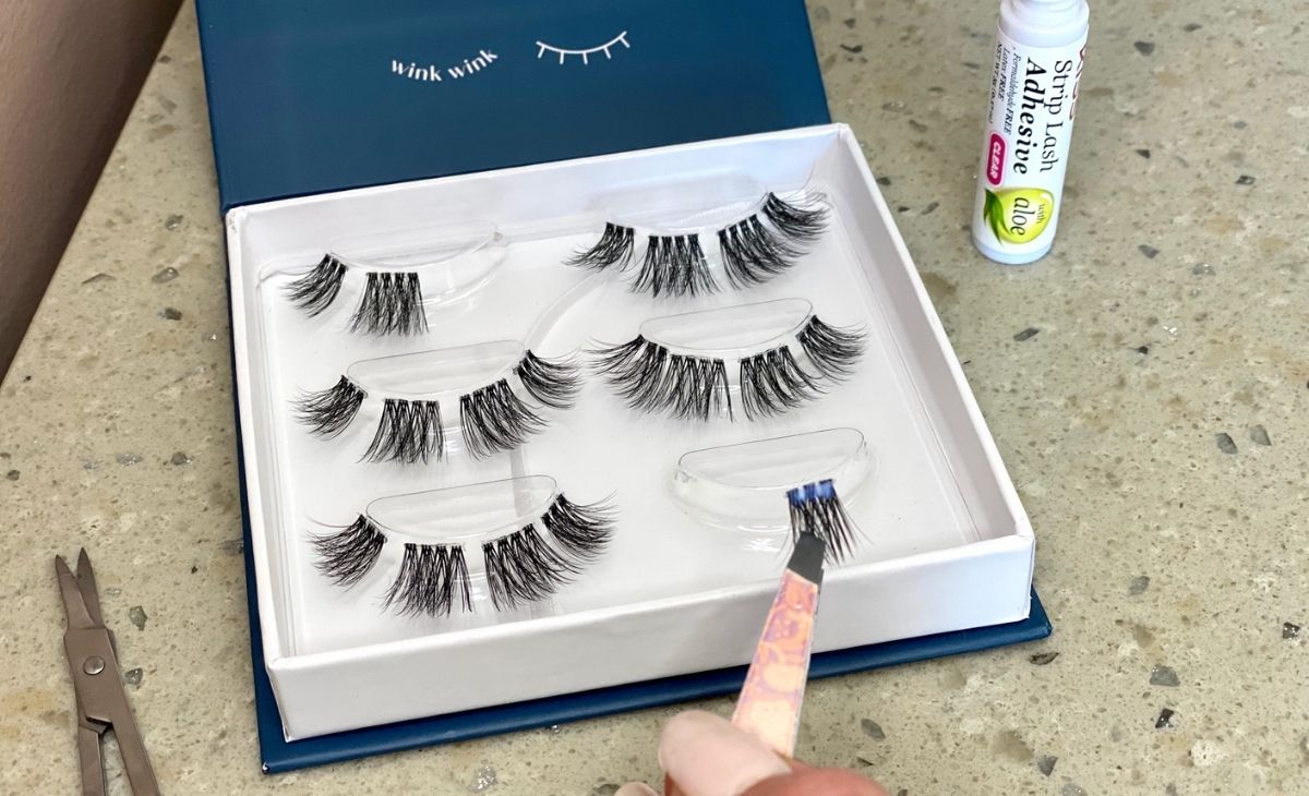 A box of false eyelashes on a counter and some tweezers with an eyelash piece on them