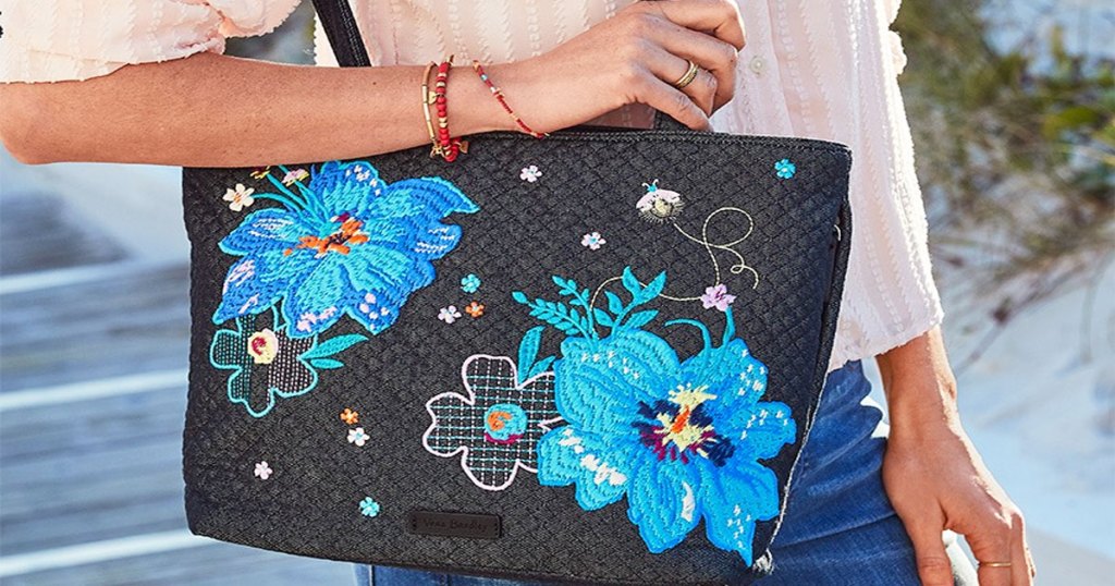 woman holding a black tote bag with two large blue flowers on it