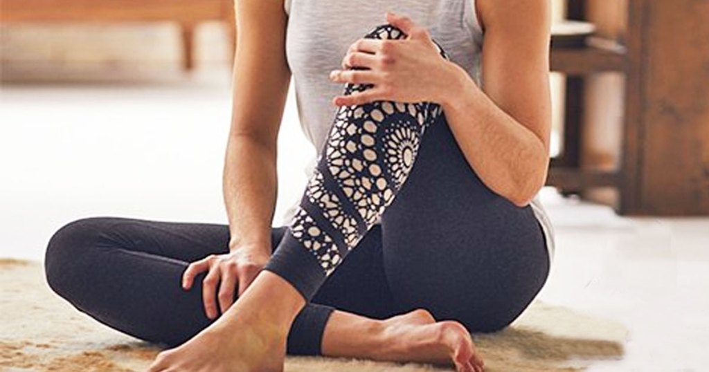 woman sitting on floor wearing white tank top and blue leggings with white mandela print on one leg