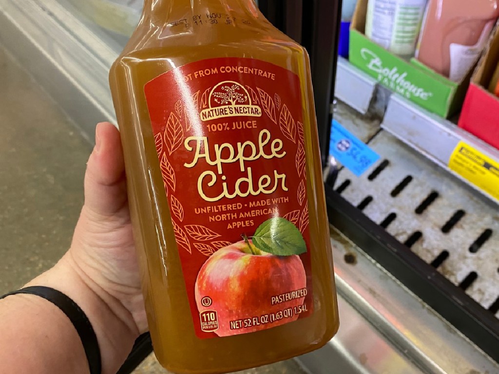 hand holding plastic bottle of apple cider near store freezer