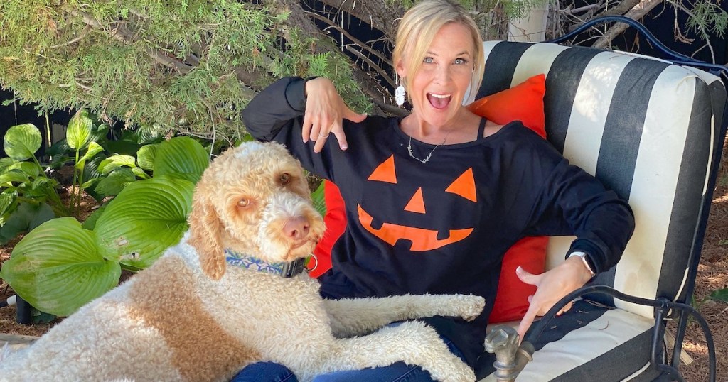 woman wearing pumpkin shirt sitting next to dog