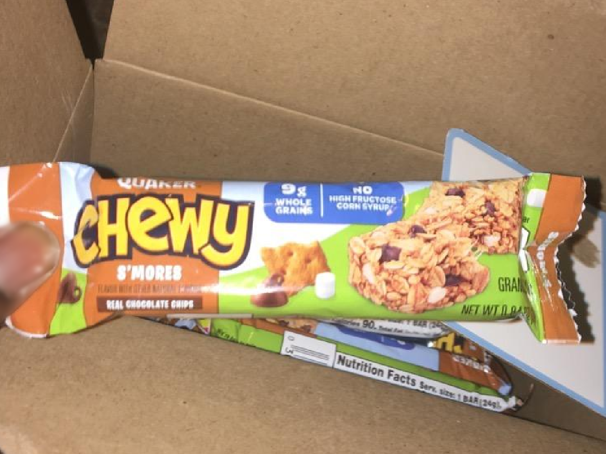 finger holding a granola bar over box