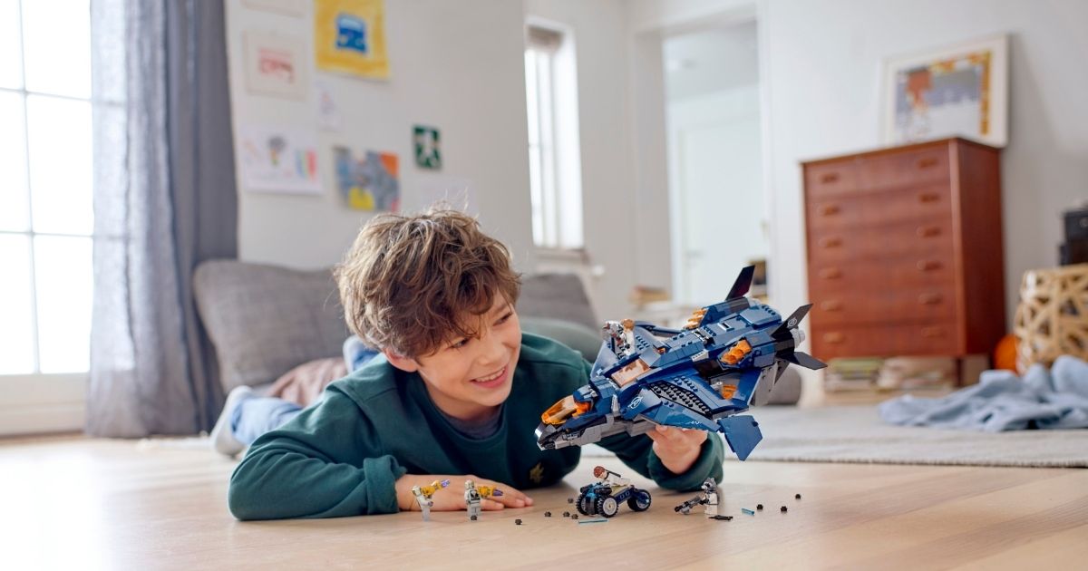 boy playing with LEGO jet and accessories on floor of room