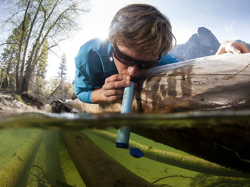 Man using a personal water filter to drink from water source outside