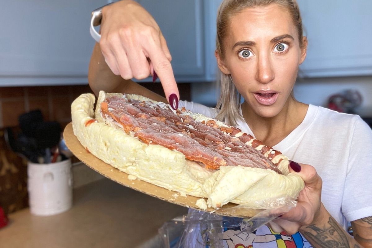 A woman holding outsiders pizza and pointing to broken crust