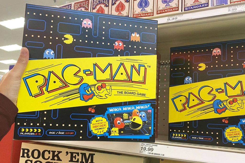 person holding up a black and yellow pac-man board game in front of target shelf