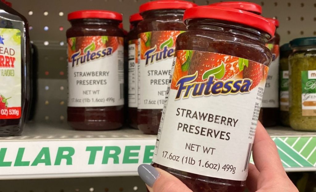 A hand holding a jar of strawberry preserves at a store