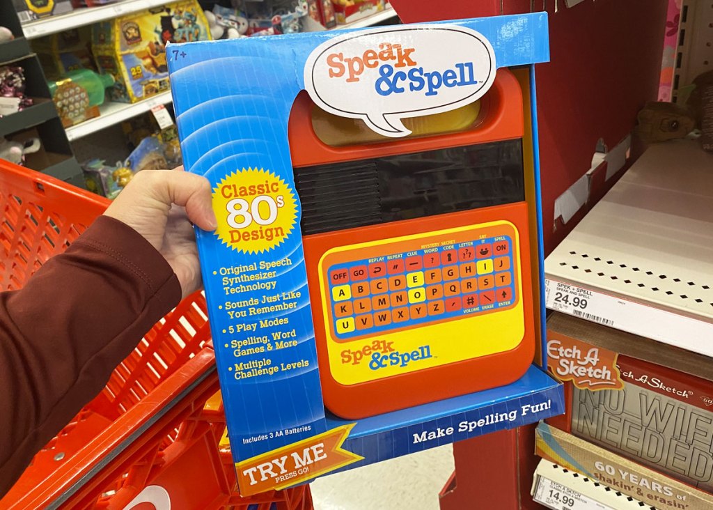 person holding up electronic speak & spell game in front of red target shopping cart