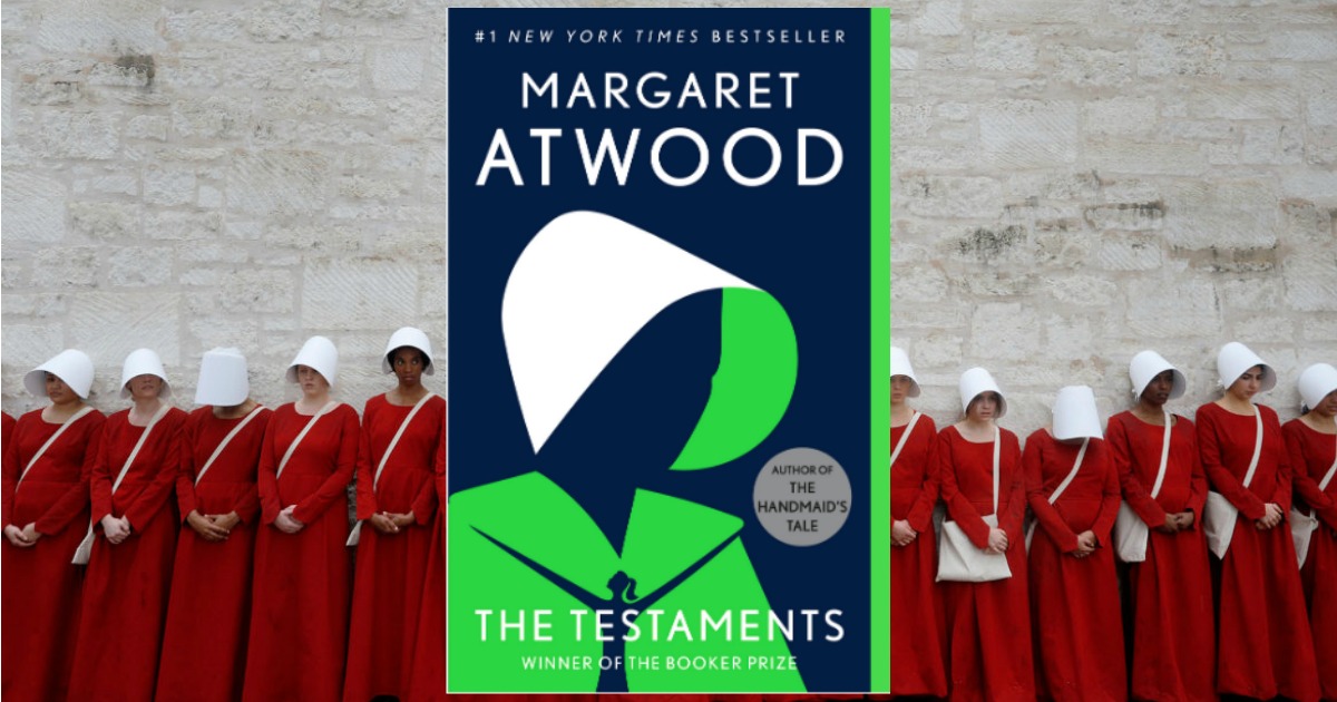 stock image of The Testaments by Margaret Atwood cover art over a picture of women in red dresses and white hats