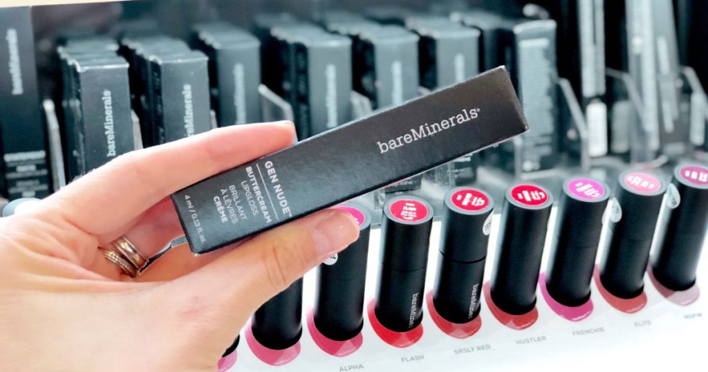 woman holding up black box for bareMinerals lipstick in front of a lipstick display