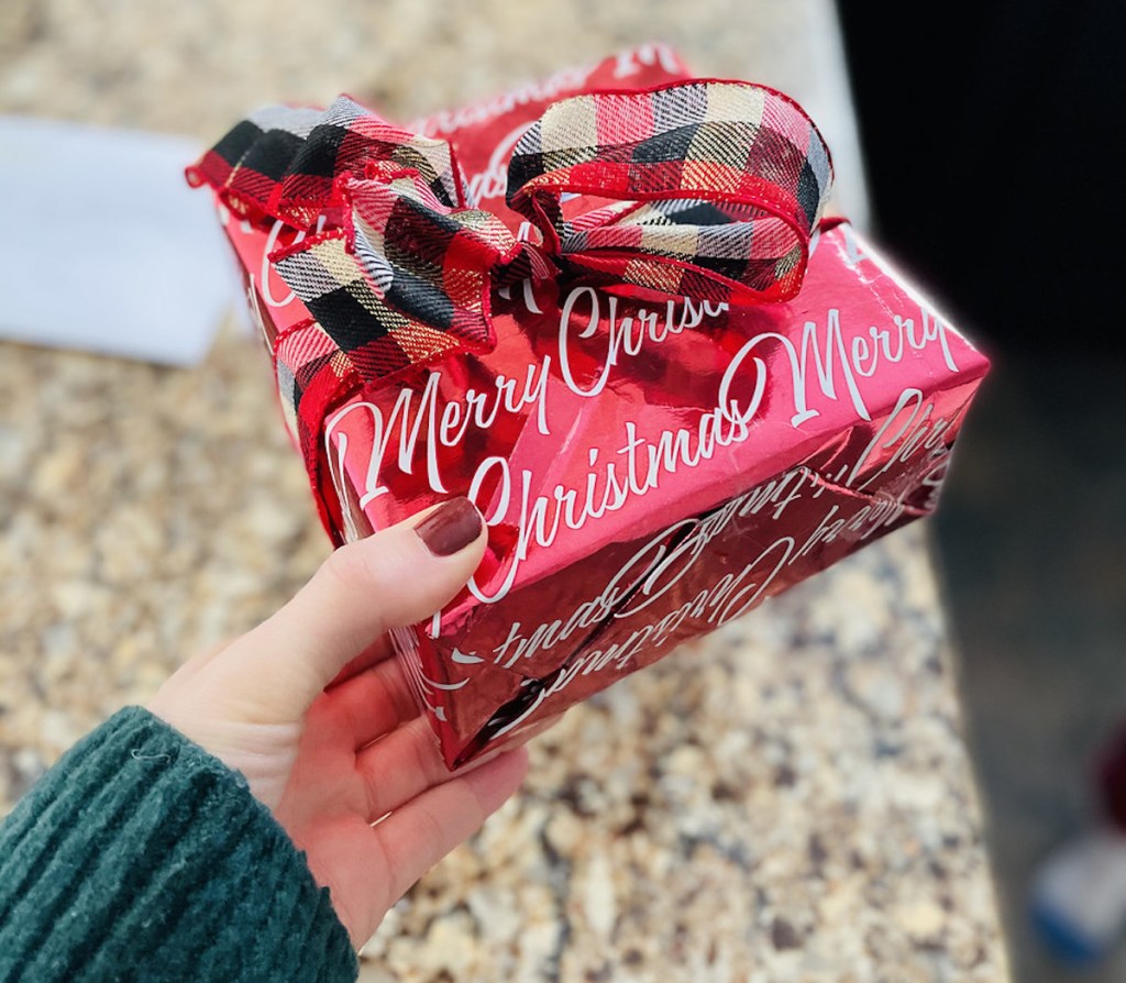 hand holding red present with merry christmas wrapping paper